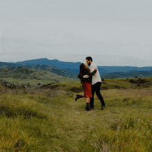 a man is holding a woman in his arms in a field with mountains in the background