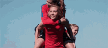 two women are carrying a woman on their shoulders on a field .