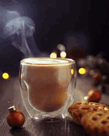 a cup of coffee with steam coming out of it is on a table next to a cookie .