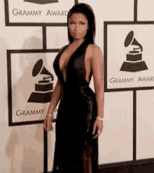 a woman in a very plunging black dress is standing in front of a wall with grammy awards logos on it .