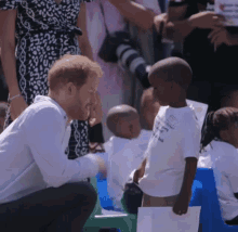 prince harry is kneeling down and talking to a young boy who is wearing a white shirt that says " i love you "