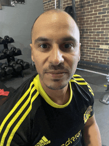 a man in a black and yellow adidas shirt looks at the camera