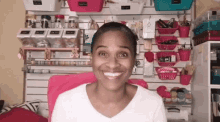 a woman is smiling while sitting in a pink chair in front of a wall with baskets on it .