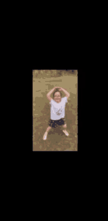 a little girl in a white shirt and blue shorts is standing on a field with her hands on her head .