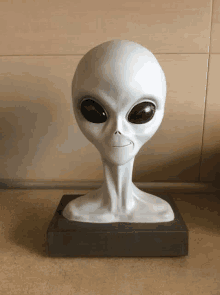 a statue of a grey alien head with black eyes is sitting on a table .