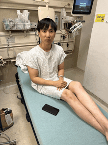 a man in a hospital gown sits on a bed with a philips monitor in the background