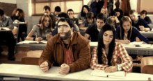 a man and a woman are sitting at a desk in a classroom with a sign that says ' classroom '