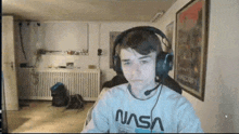 a young man wearing headphones and a nasa shirt looks at the camera