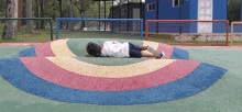 a child laying on a rainbow colored surface in a park