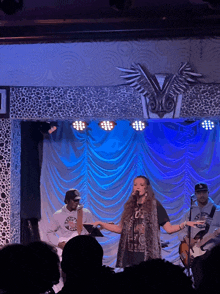 a woman singing into a microphone on a stage in front of a blue curtain