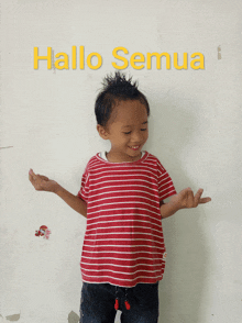 a young boy in a red and white striped shirt is standing in front of a wall that says hallo semua