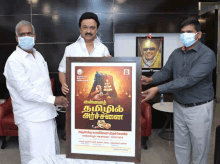 a man wearing a mask is holding a framed poster with tamil writing on it