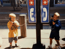 a boy wearing a yellow shirt with the word ona on it talks on a pay phone