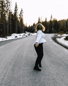 a woman in a white top and black pants is dancing on the road