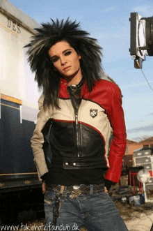 a man in a red and white leather jacket is standing in front of a trailer that says des