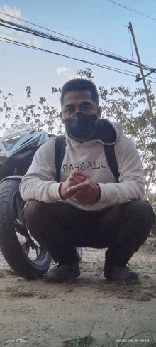 a man wearing a mask squats in front of a motorcycle