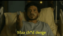 a man is laying in a hospital bed holding a remote control with the words maa ch * d denge above him .