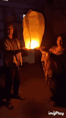 a man and a woman are holding a lantern in their hands and the lantern is lit up in the dark