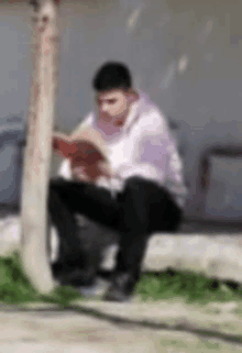 a blurry picture of a man reading a book while sitting under a tree .