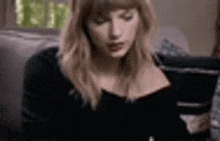 a woman in a black shirt is sitting on a couch looking at her phone .