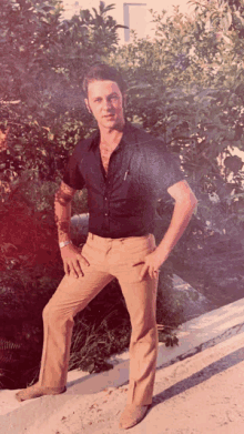 a man in a black shirt and tan pants is standing in front of a bush