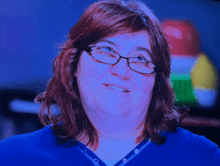 a woman wearing glasses and a blue shirt smiles at the camera