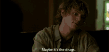 a man with curly hair is sitting in a dark room and says maybe it 's the drugs