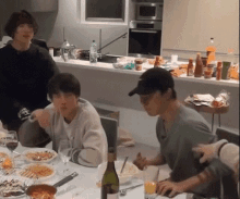 a group of people are sitting at a table in a kitchen eating food .