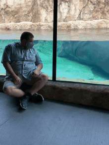 a man wearing a mask sits in front of a hippopotamus exhibit