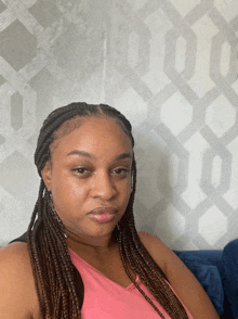 a woman with braids is sitting in front of a wall with a geometric pattern