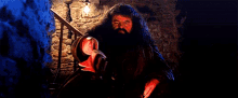 a man with a beard is standing in front of a fireplace holding a sword .