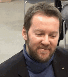 a man with a beard is wearing a blue turtleneck and a black jacket