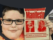 a boy wearing glasses holds up a pamphlet that says communism manifesto