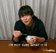 a man sitting at a table with a spoon in his mouth and the words " i 'm not sure what it is " above him