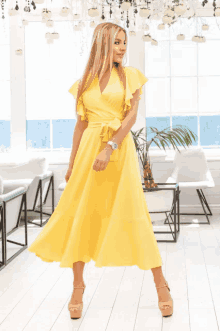 a woman in a yellow dress with ruffled sleeves is standing in front of a window