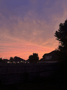 a sunset with a fence in the foreground and a few houses in the background