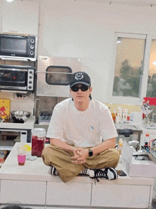 a man sitting on a counter wearing a black hat that says ' a.r.c. ' on it