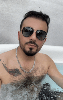 a man in a bathtub wearing sunglasses and a feather tattoo on his chest