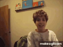 a young boy with curly hair is smiling in front of a wall with a shelf of books on it .