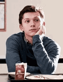 a young man is sitting at a table with his hand on his chin and a carton of borden milk next to him .