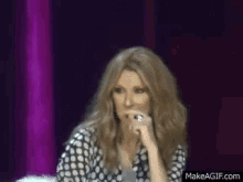 a woman in a polka dot shirt is holding a microphone in front of a purple curtain .