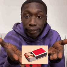 a man in a purple hoodie is holding a box of matches in his hands