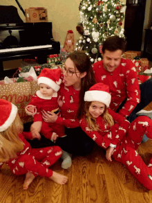 a family sitting on the floor in front of a christmas tree with a merry christmas bag in the background