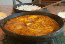 a bowl of food with a wooden spoon in it sits on a table next to a bowl of rice