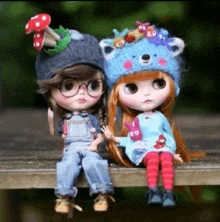 two dolls are sitting on a wooden bench .