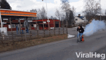 a man is riding a scooter with smoke coming out of it in front of a gas station that says din