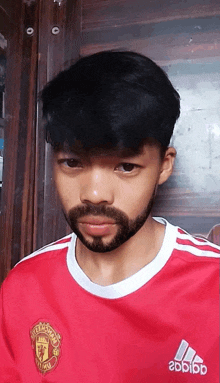 a young man with a beard is wearing a red adidas shirt