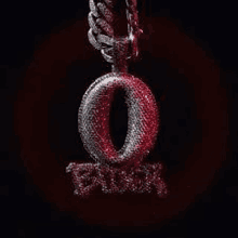 a pendant with the letter o on it is hanging from a chain on a black background .