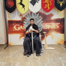 a man sitting on a throne with a sword in front of a game of thrones banner