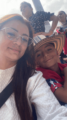 a woman wearing glasses stands next to a boy wearing a hat that says ' x ' on it